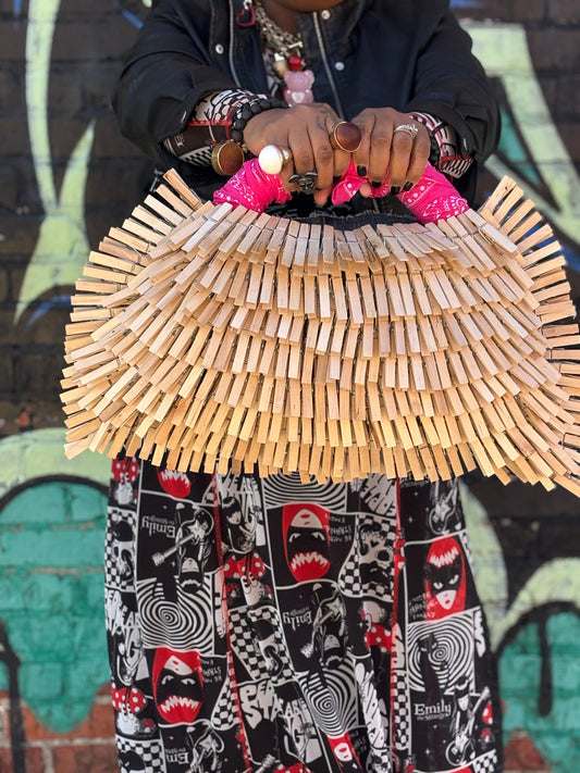 Woman holding a funky handmade clothespin bag with a pink bandanna handle, standing in front of a graffiti wall, wearing bold accessories and expressive personal style
