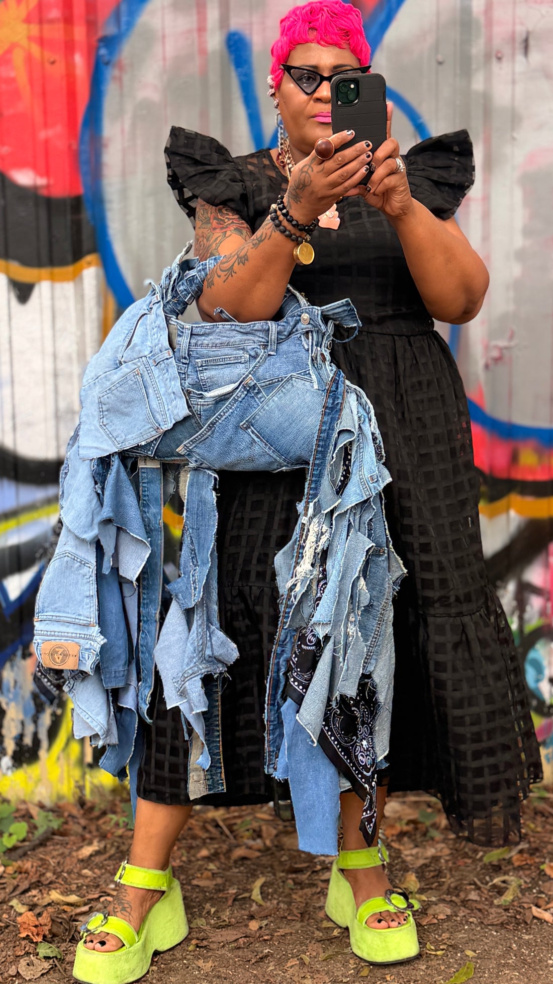 Tangie carrying Denim Overload, a layered jean-pocket handbag with long denim and black bandana fringe, styled with a black dress and lime-green platform sandals.