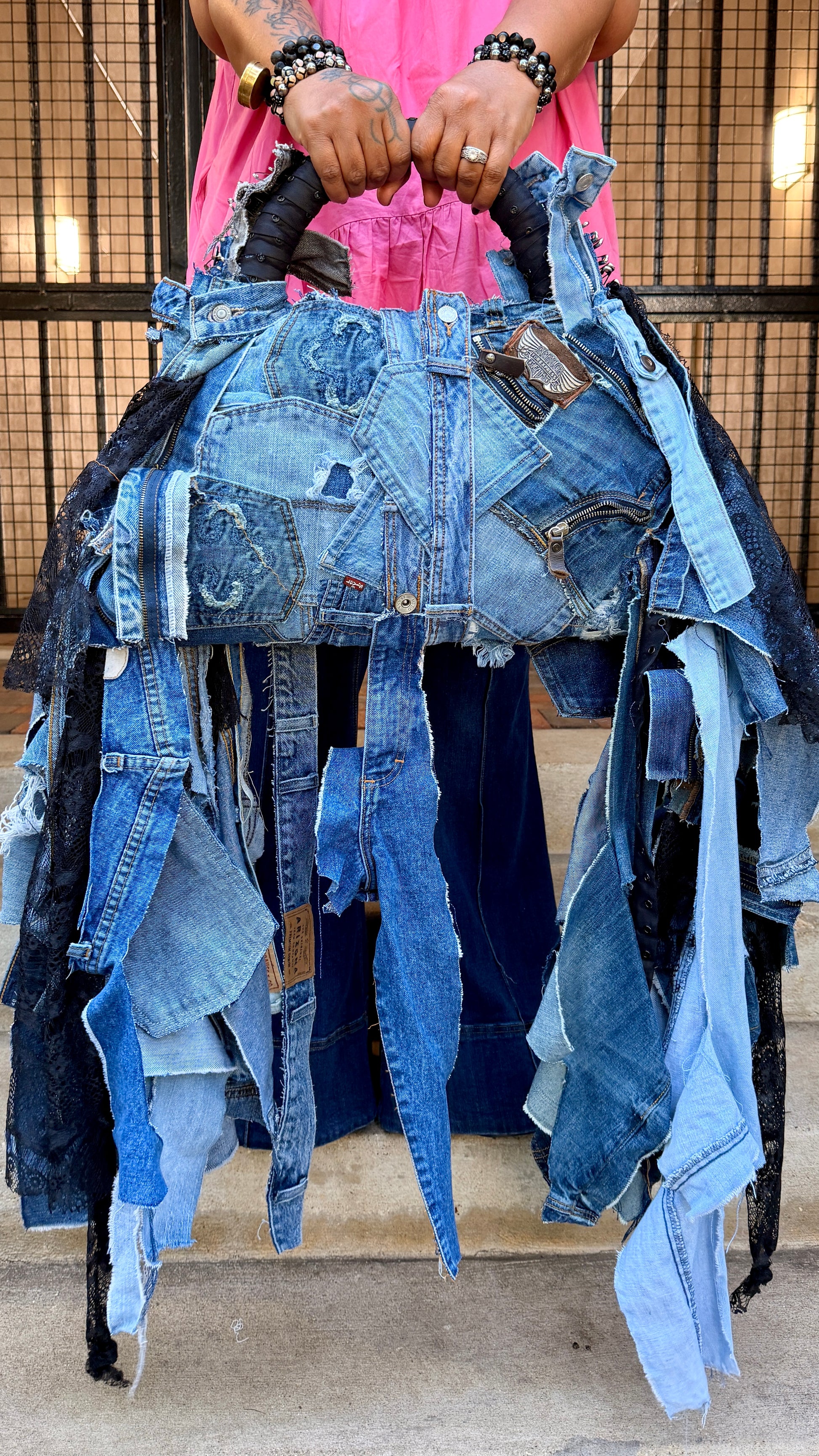 Upcycled denim on denim statement bag with shaggy frayed strips, black bandana details, patchwork denim, and black handheld handle.