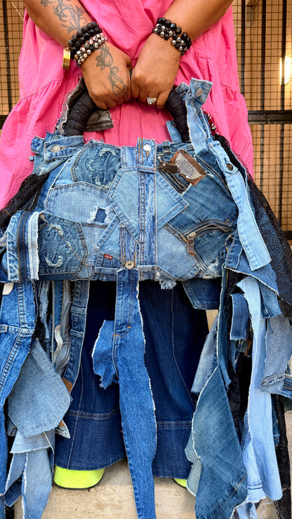 Close-up of upcycled denim bag with black and gray patchwork, distressed denim edges, and visible jeans label detail.