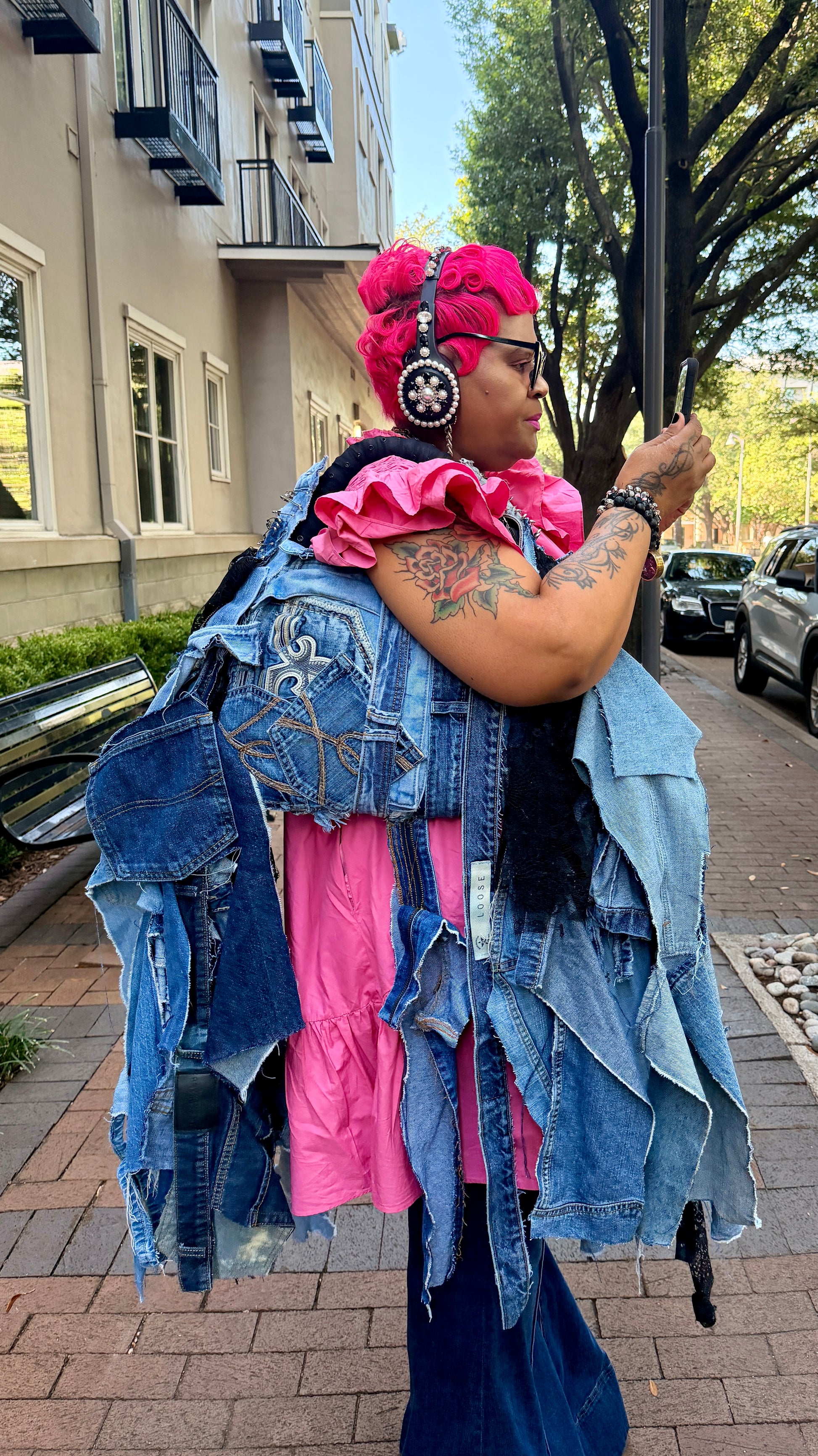 Person wearing a colorful outfit with denim bag and pink elements on a street.