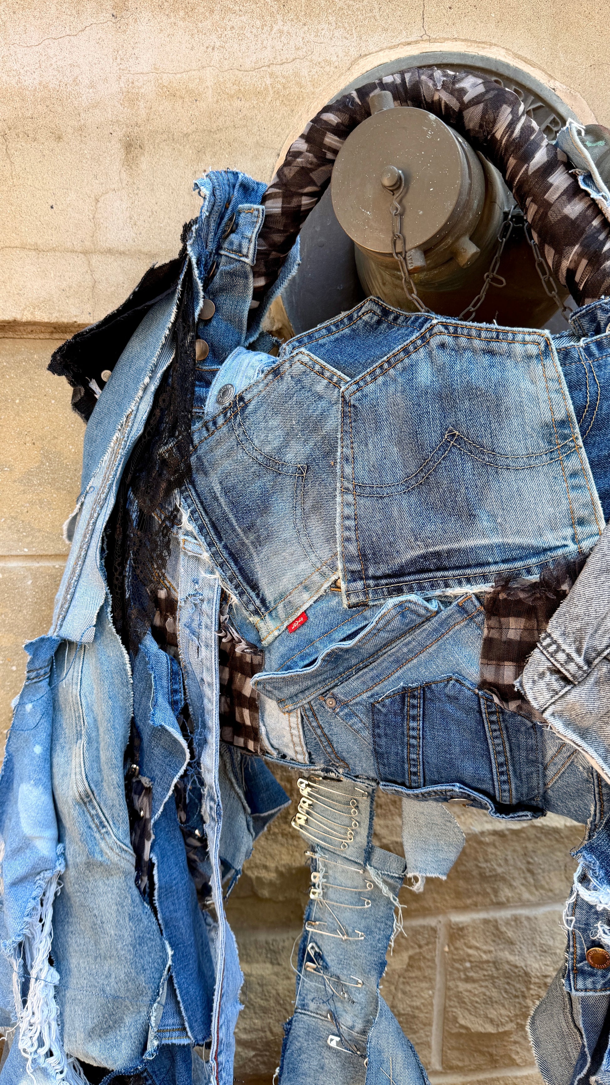 Front view of handmade upcycled denim statement bag with long hanging strips, patchwork denim, plaid accents, and mixed textures.