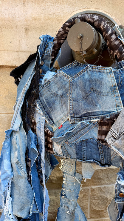 Front view of handmade upcycled denim statement bag with long hanging strips, patchwork denim, plaid accents, and mixed textures.