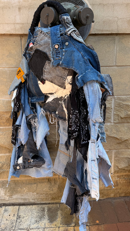 Upcycled denim on denim performative style bag with shaggy frayed strips, black bandana details, patchwork denim, and black handheld handle.