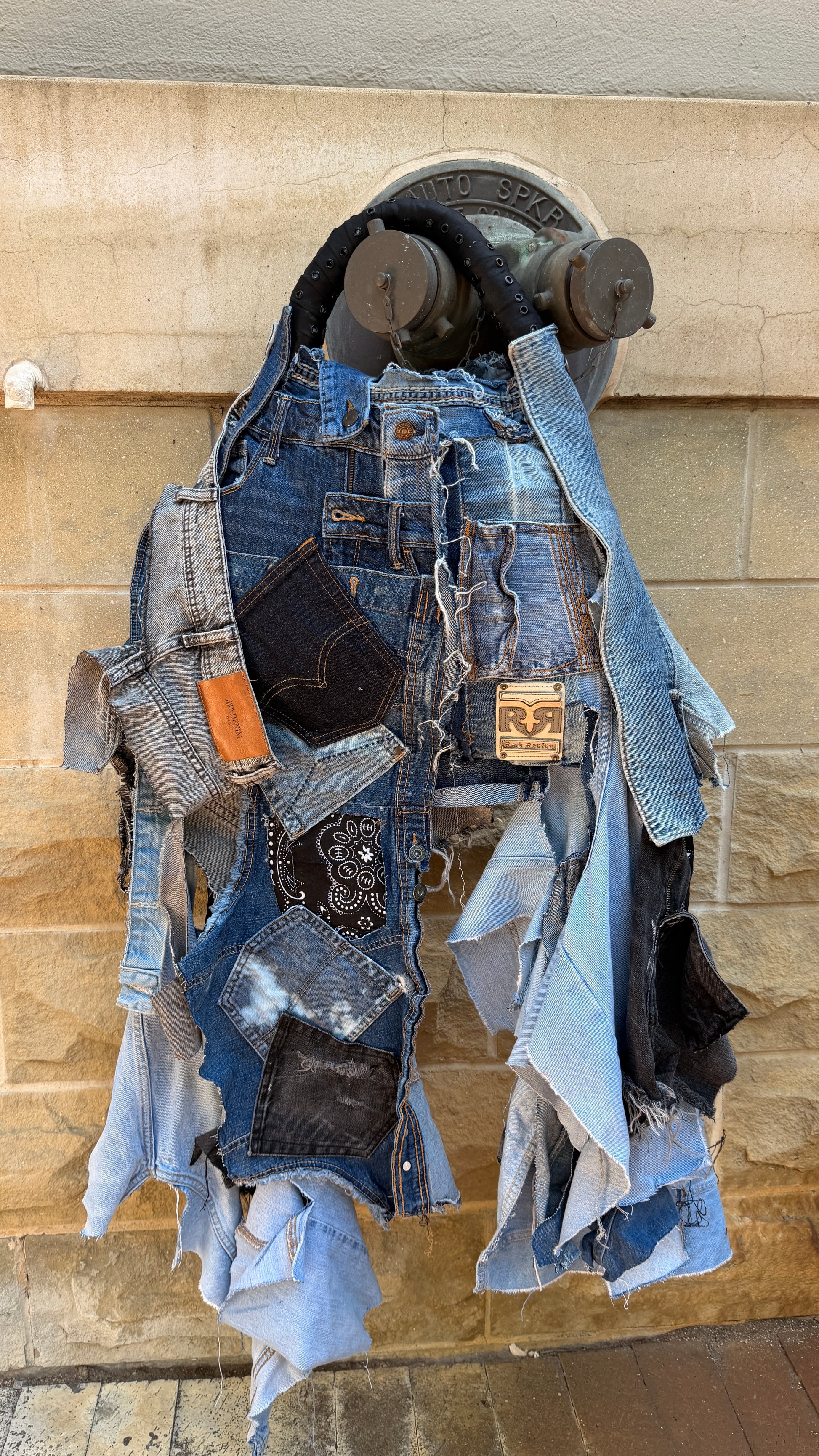 Close-up of denim patchwork bag with black and gray fabric pieces, frayed edges, and visible jeans label.