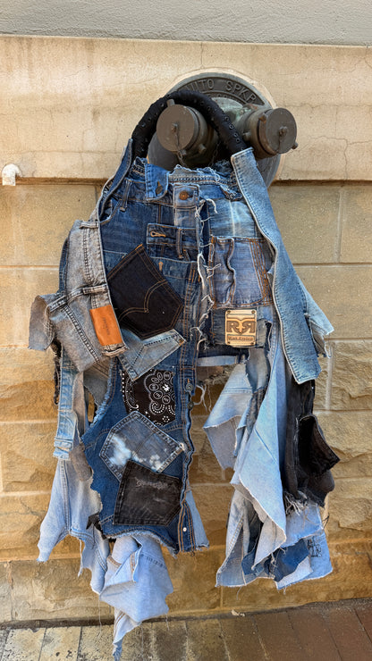 Close-up of denim patchwork bag with black and gray fabric pieces, frayed edges, and visible jeans label.