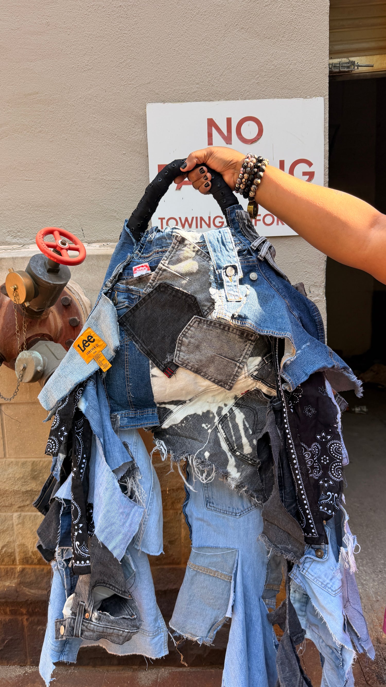 Hand holding a pile of denim bag items with a 'No Towing' sign in the background.