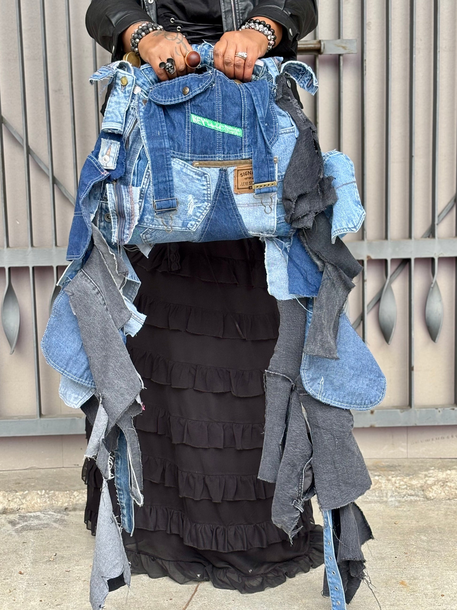 Person holding a denim jacket with layered clothing items against a wooden fence background