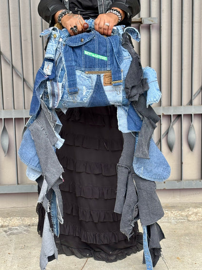 Person holding a denim jacket with layered clothing items against a wooden fence background