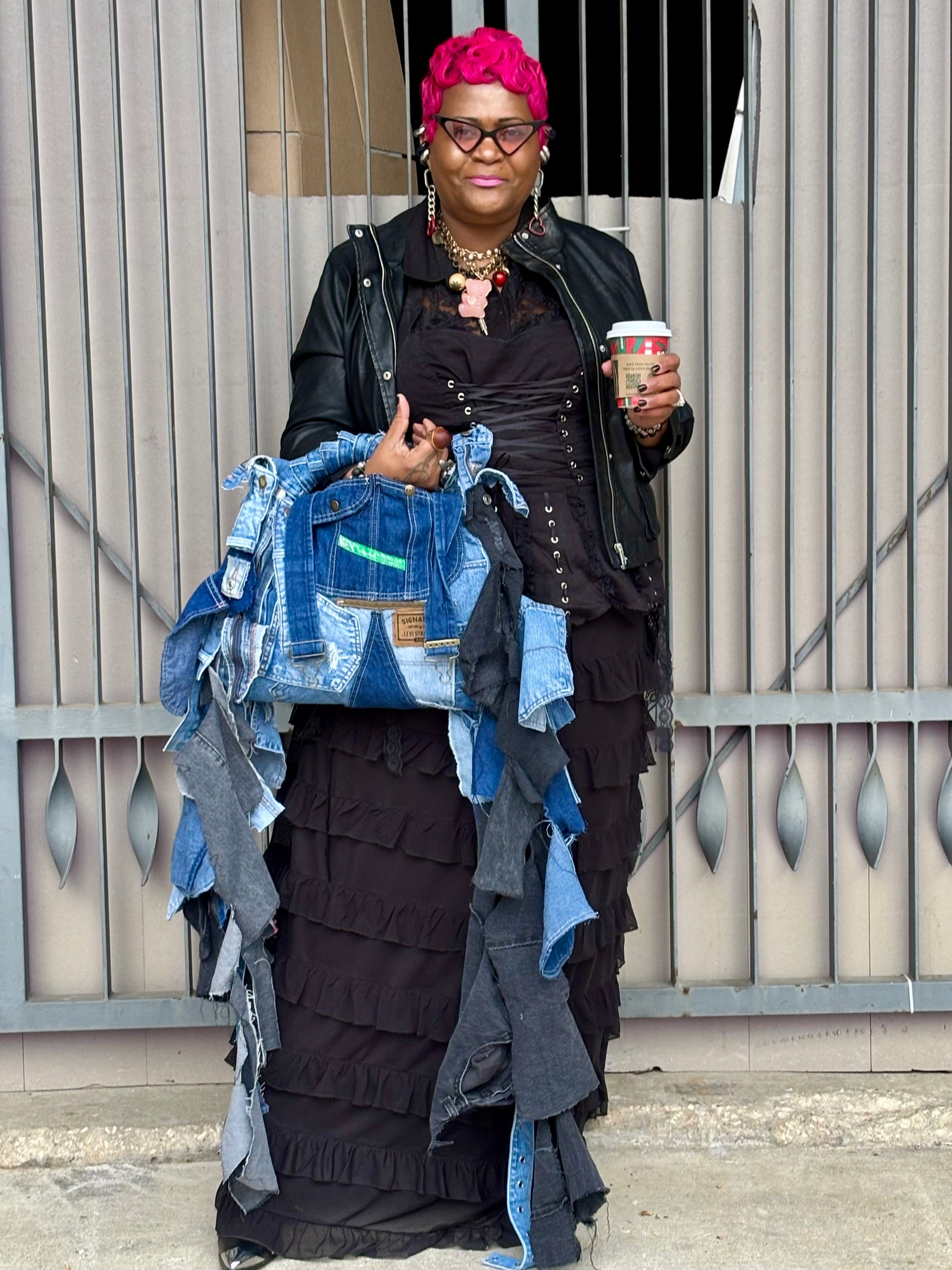 Woman holding a denim jacket and a coffee cup, standing against a neutral background