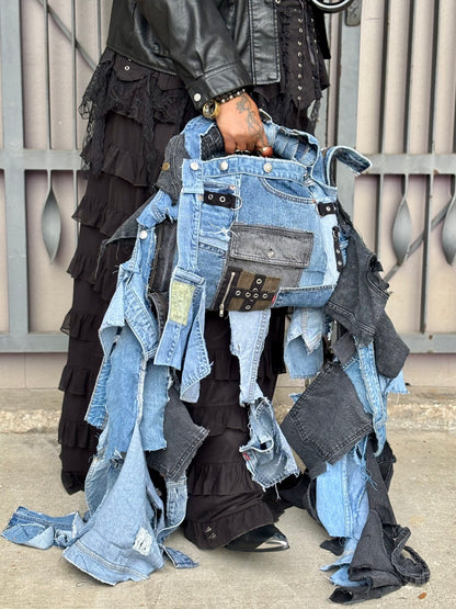 Person holding a collection of denim bag with a metallic fence background