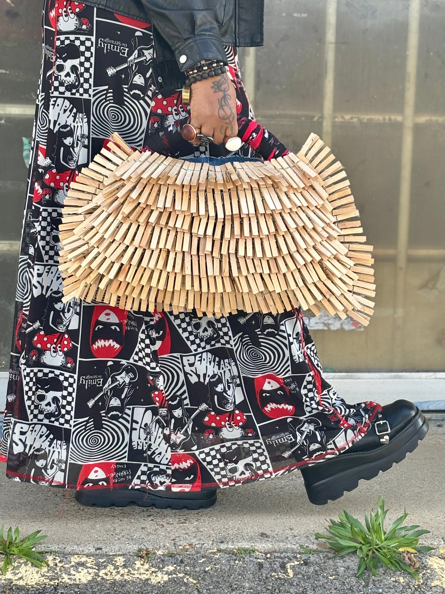 Person wearing a patterned skirt and holding a clothespin denim bag on a street.