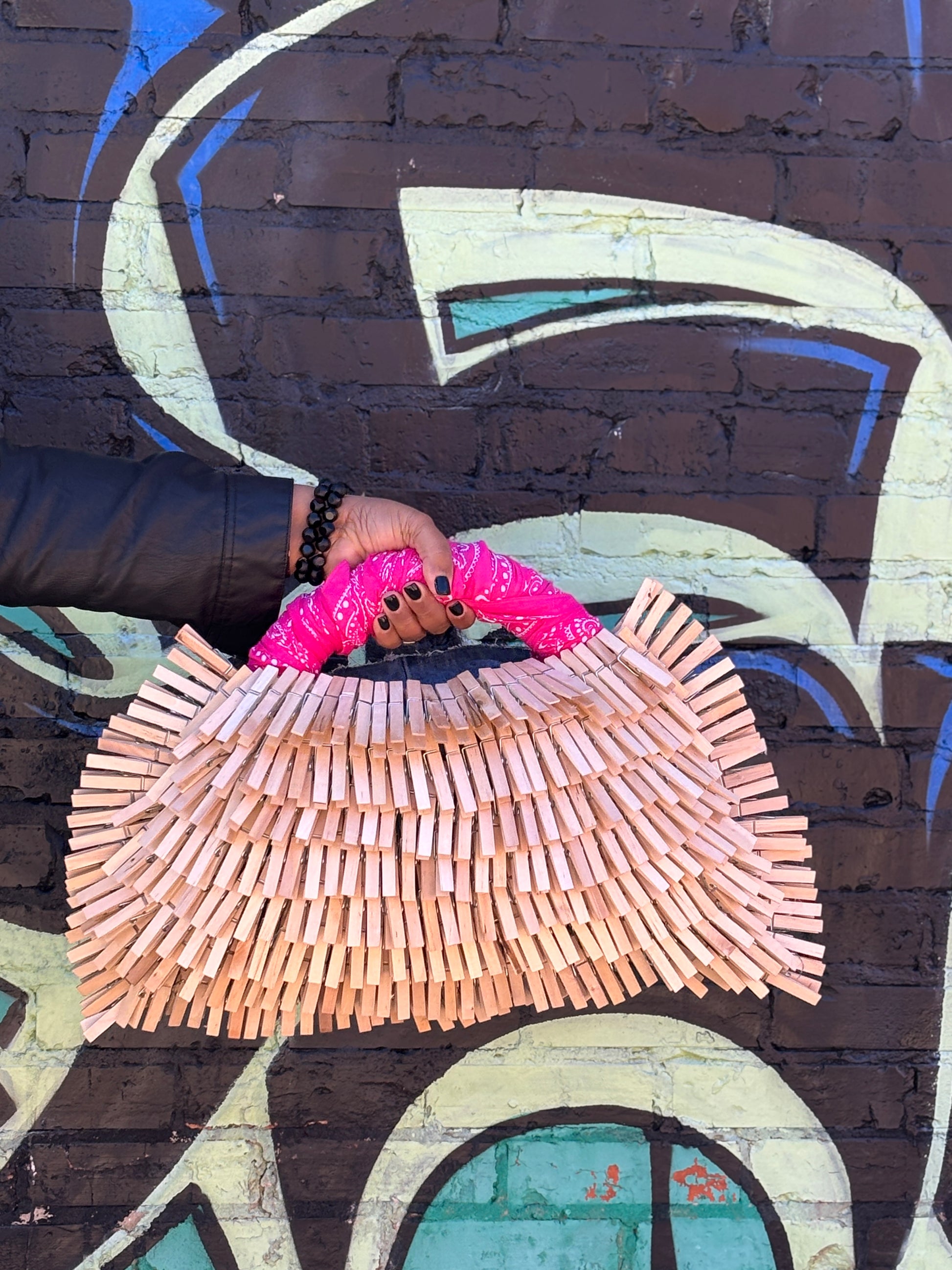 Handmade bag made of wooden clothespins held against a graffiti-covered wall.