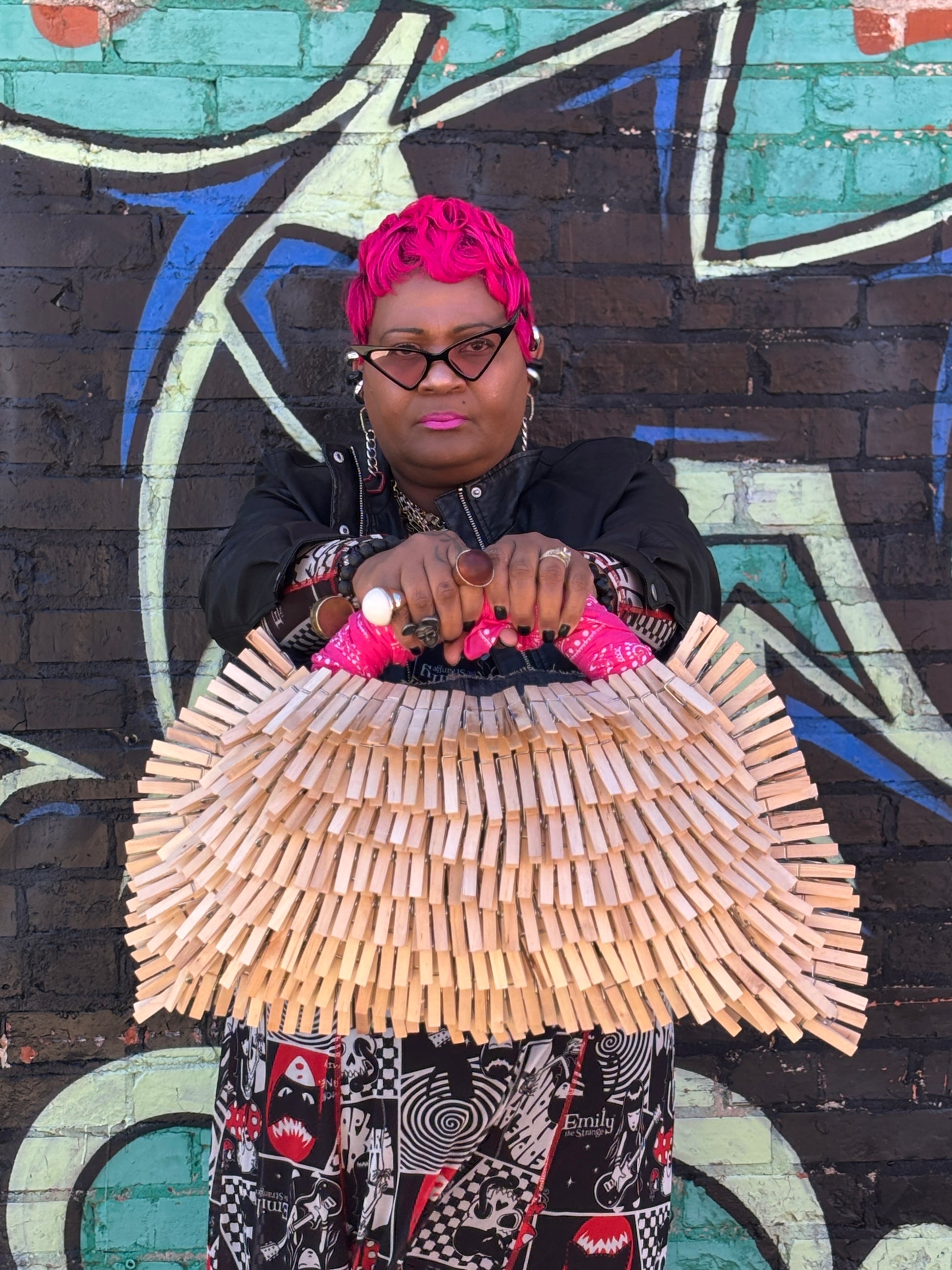 Person holding a unique pink clothespin denim denim handbag against a colorful graffiti wall.