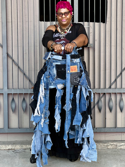 Tangie Bell with pink hair showing off denim ugly bag with a black top standing against a metal gate.